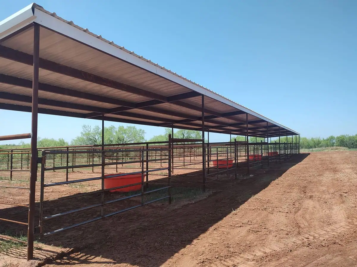 Inside a covered steel working-pen barn with red pipe fencing