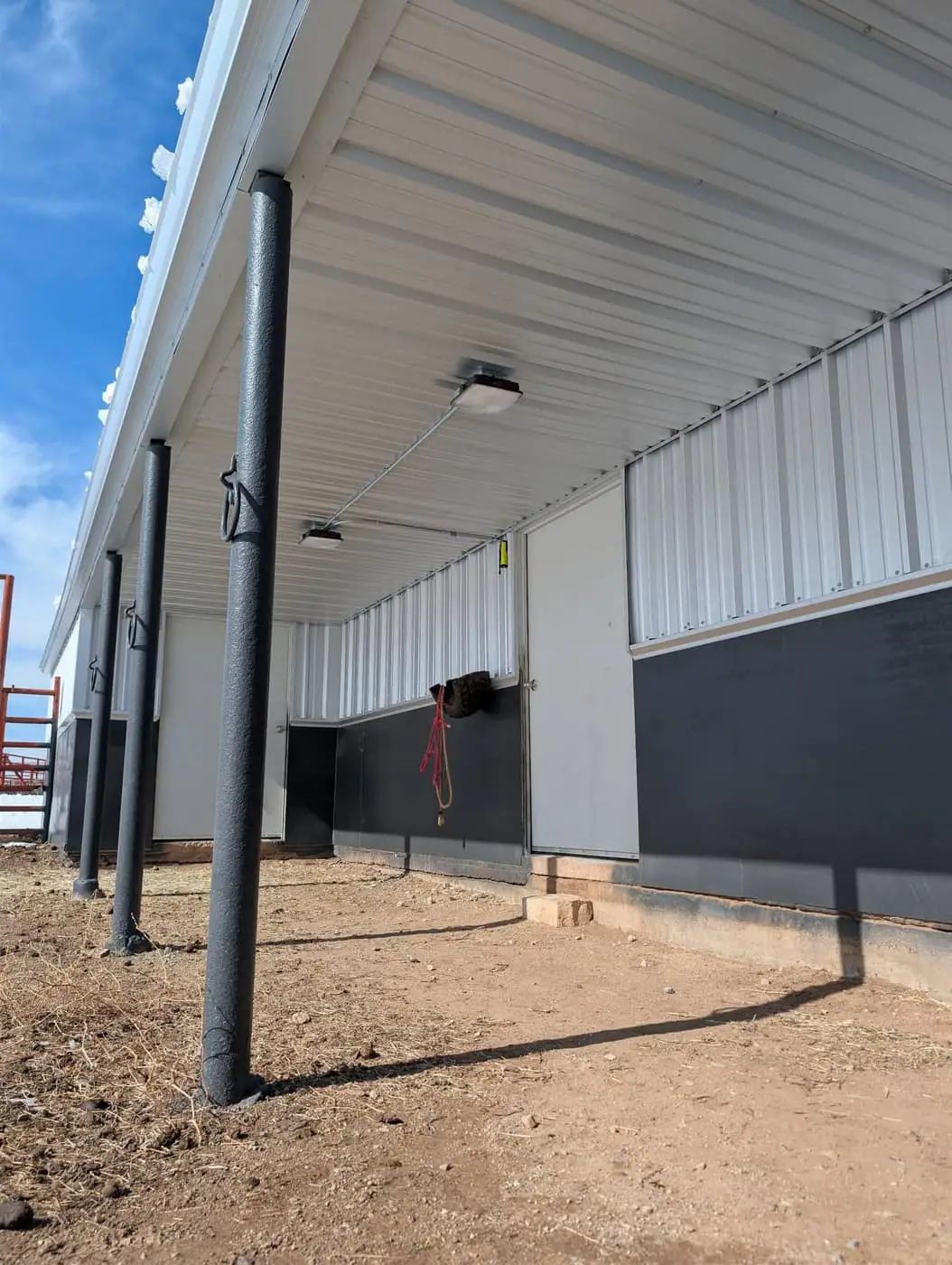 Covered porch on a white steel barn with dark wainscot and black posts