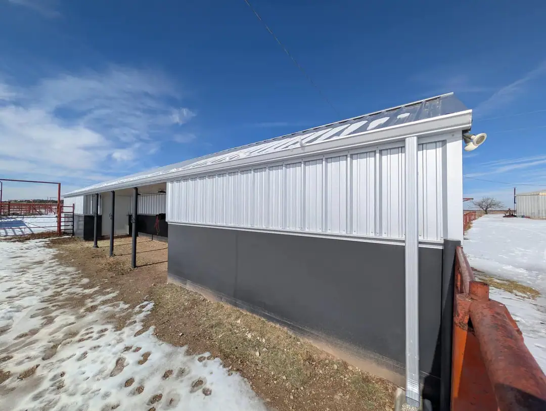 White steel barn with a dark base and a covered side porch on a snowy day