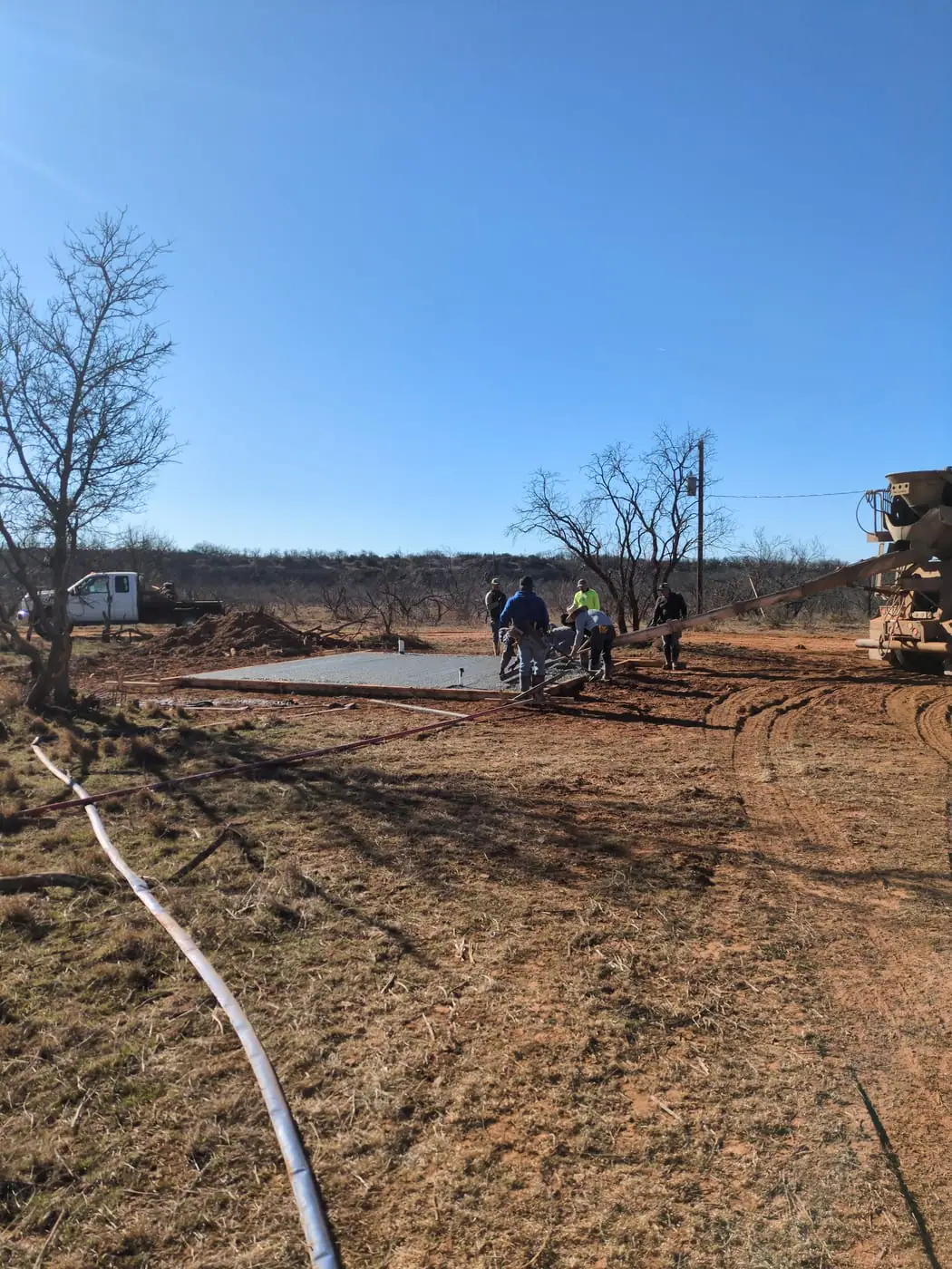Concrete truck chute pouring a slab while the crew screeds it under a clear blue sky