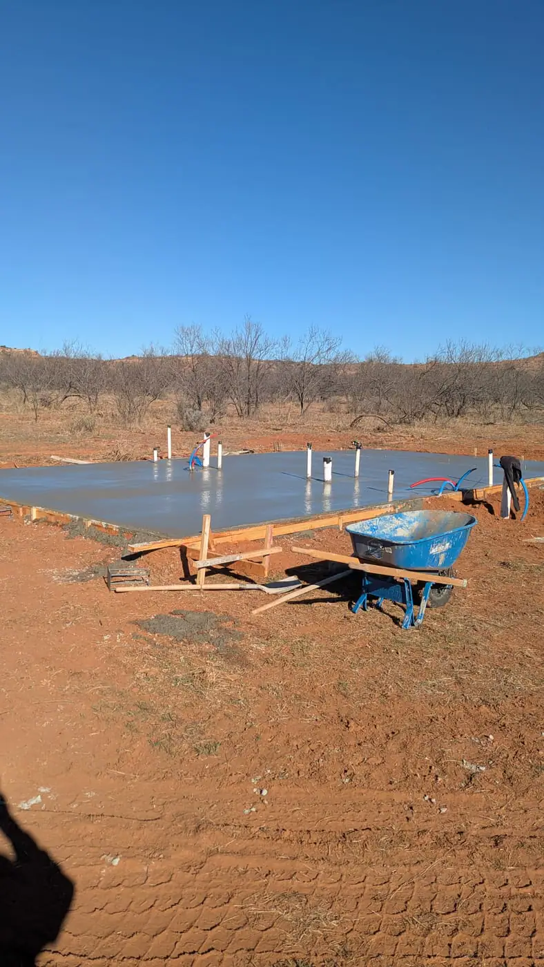 Freshly poured slab with plumbing stub-ups and a wheelbarrow in front