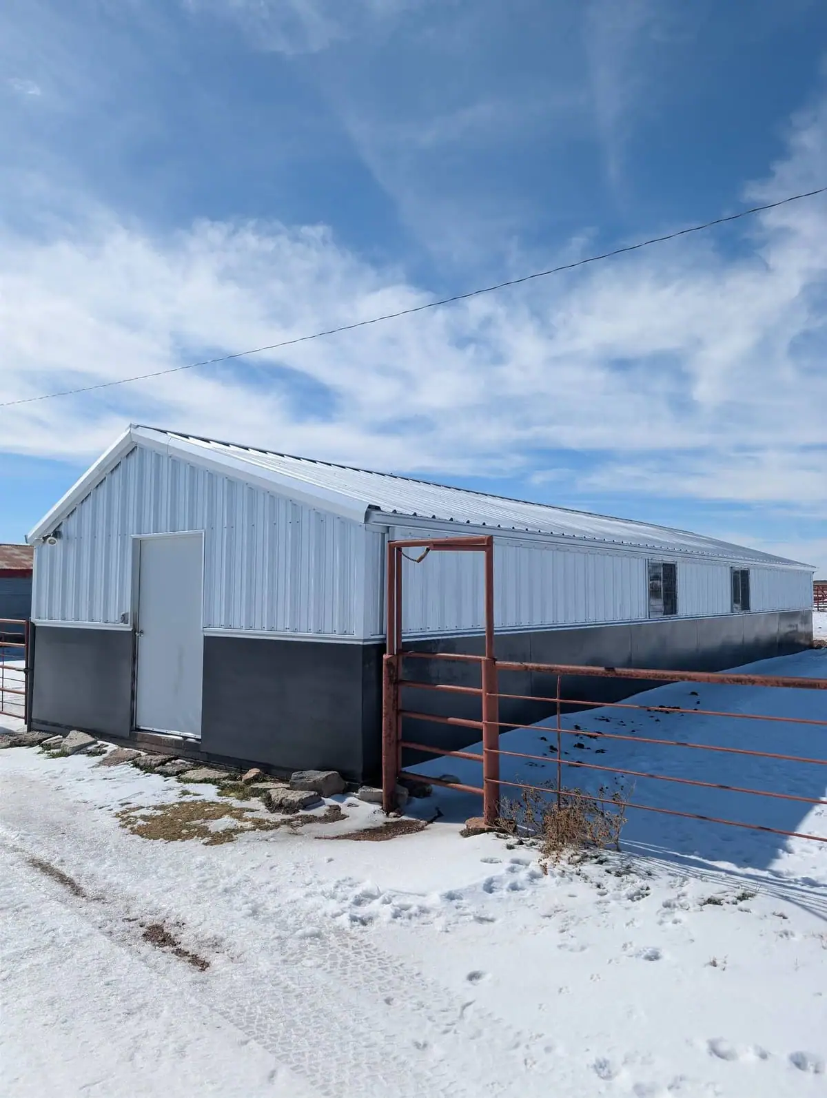 White steel shop with a dark wainscot and red pipe fence in the snow