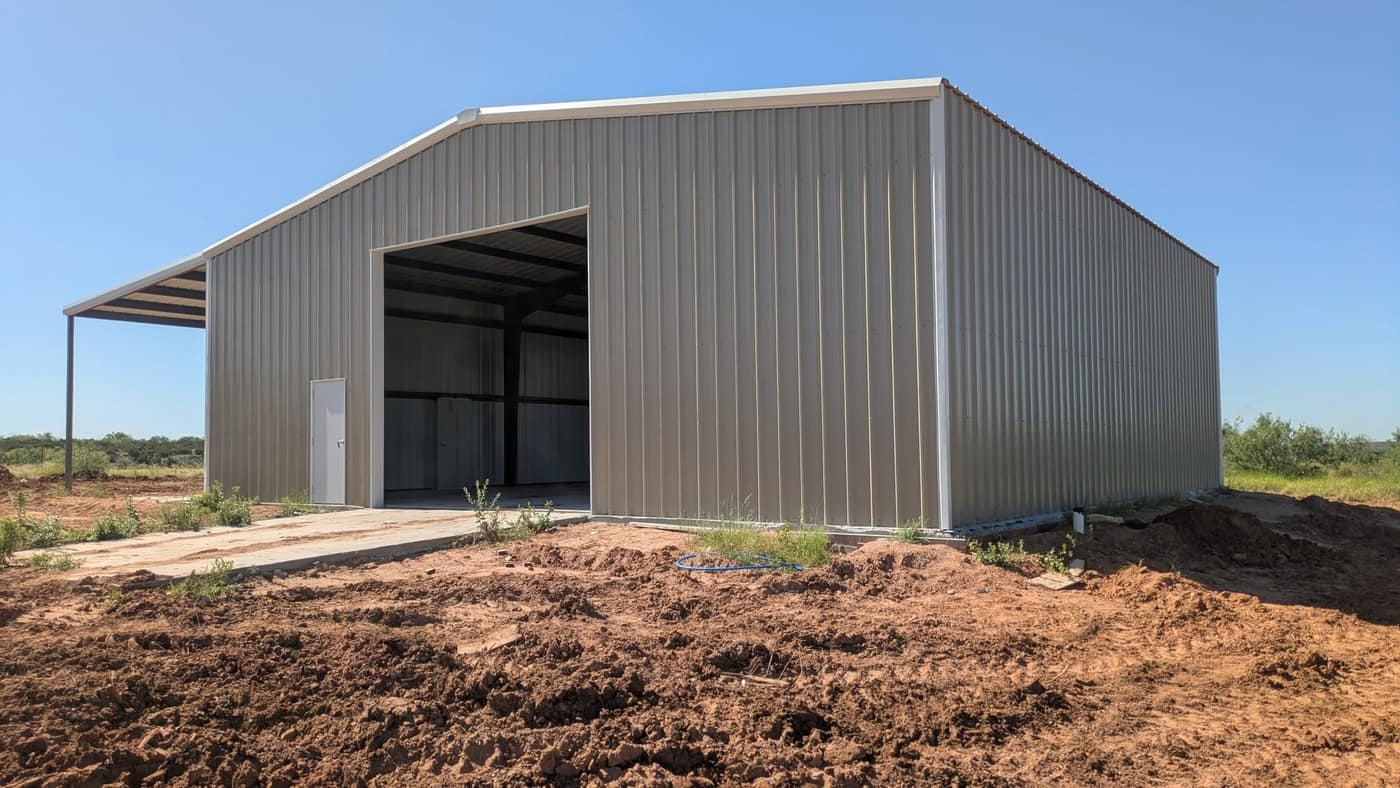 Tan steel shop with a tall open bay door on fresh-graded ground