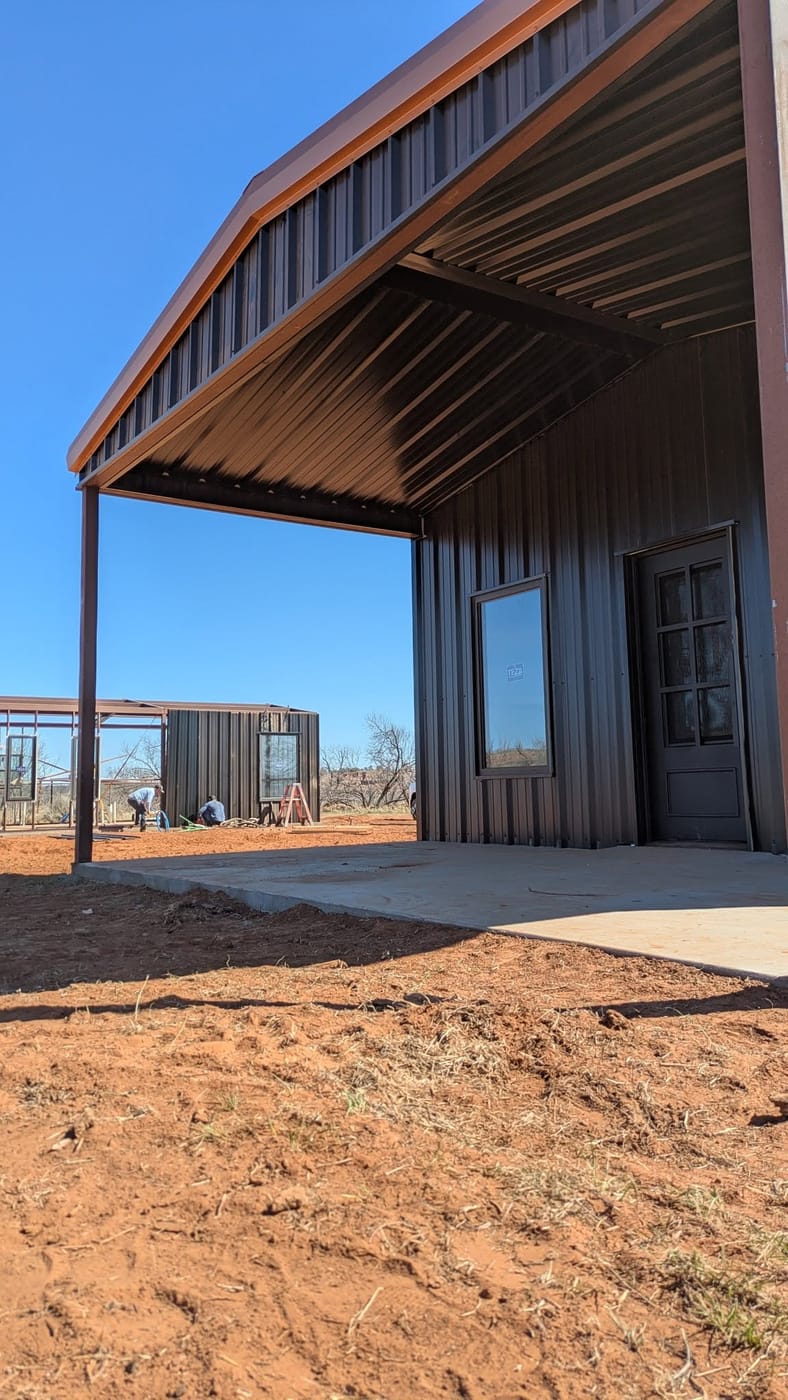 Dark brown steel building with a deep covered porch on a concrete slab