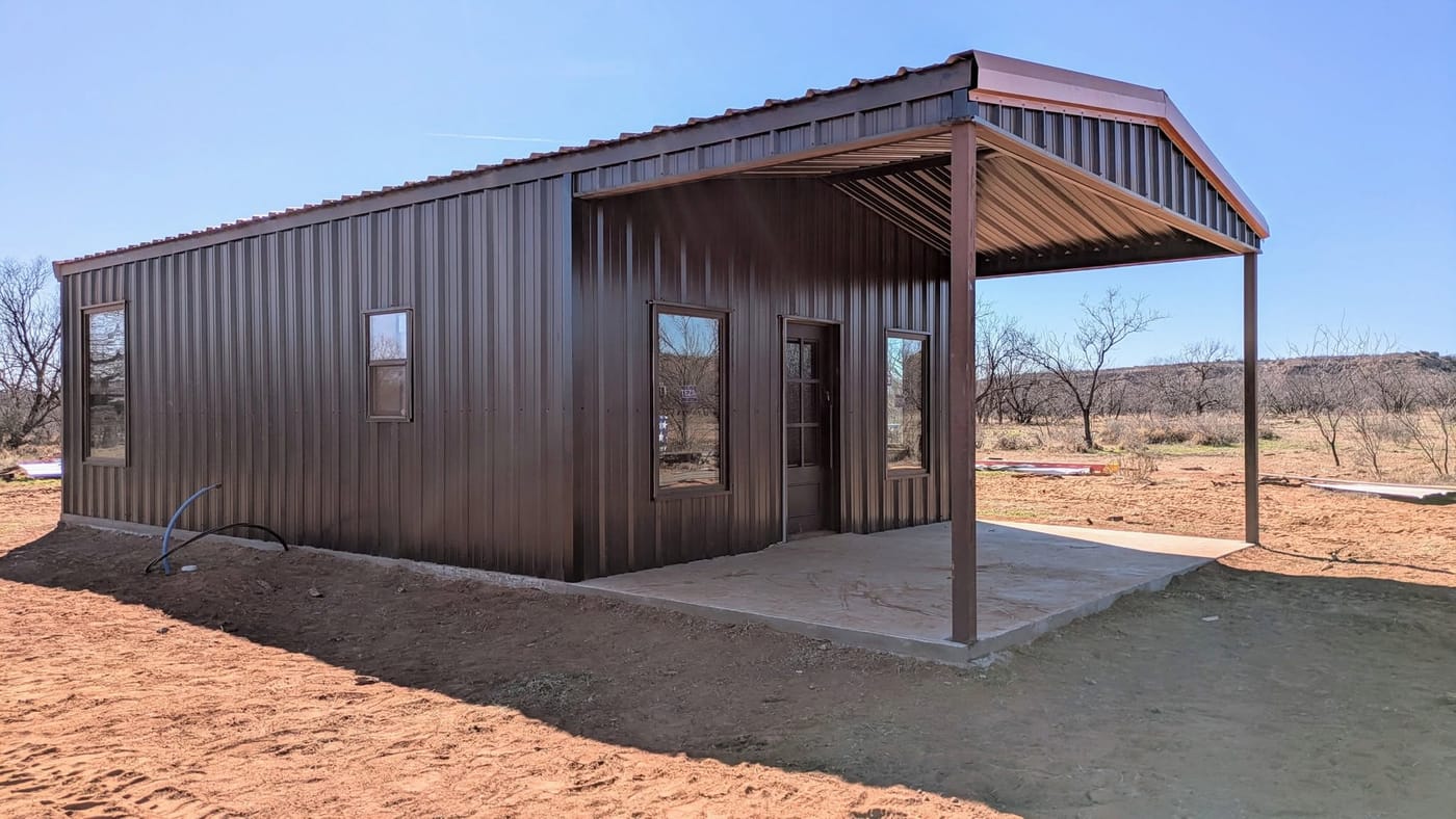 Dark brown steel home with a covered porch on freshly graded red dirt