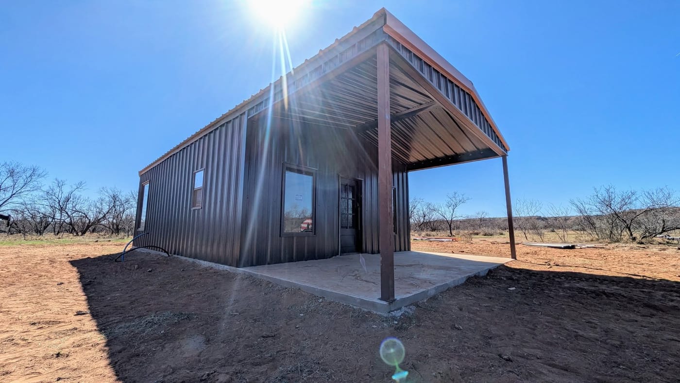 Dark brown steel building with an open porch, seen from the yard