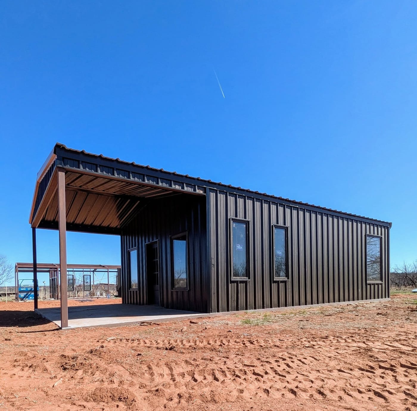 Dark steel home with a covered porch and tall windows on red dirt
