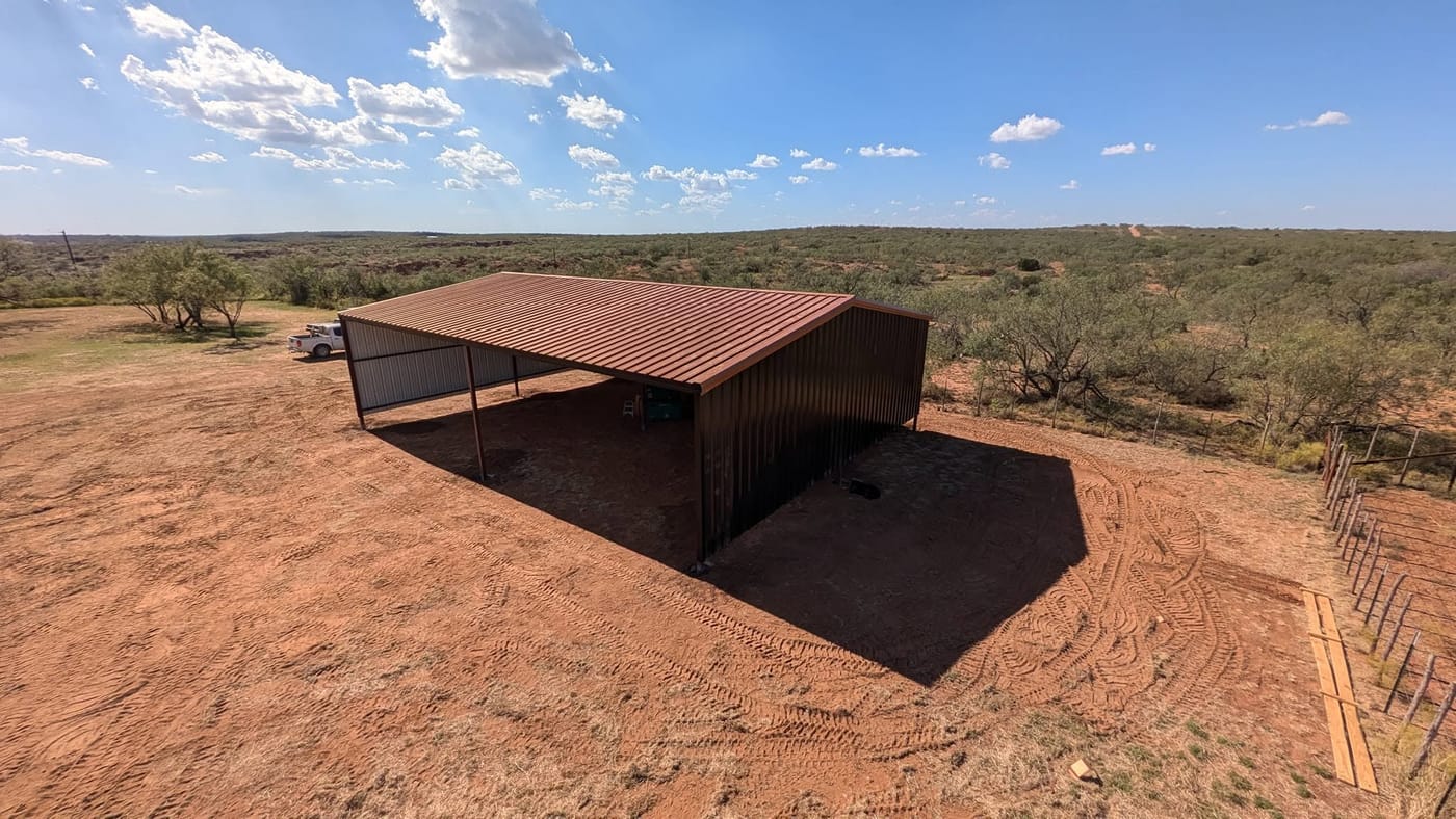 Open-sided steel loafing shed with a brown roof on open ranch land