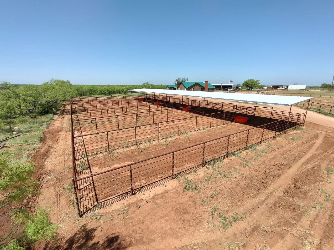 Pipe fence pens laid out on red dirt, seen from above