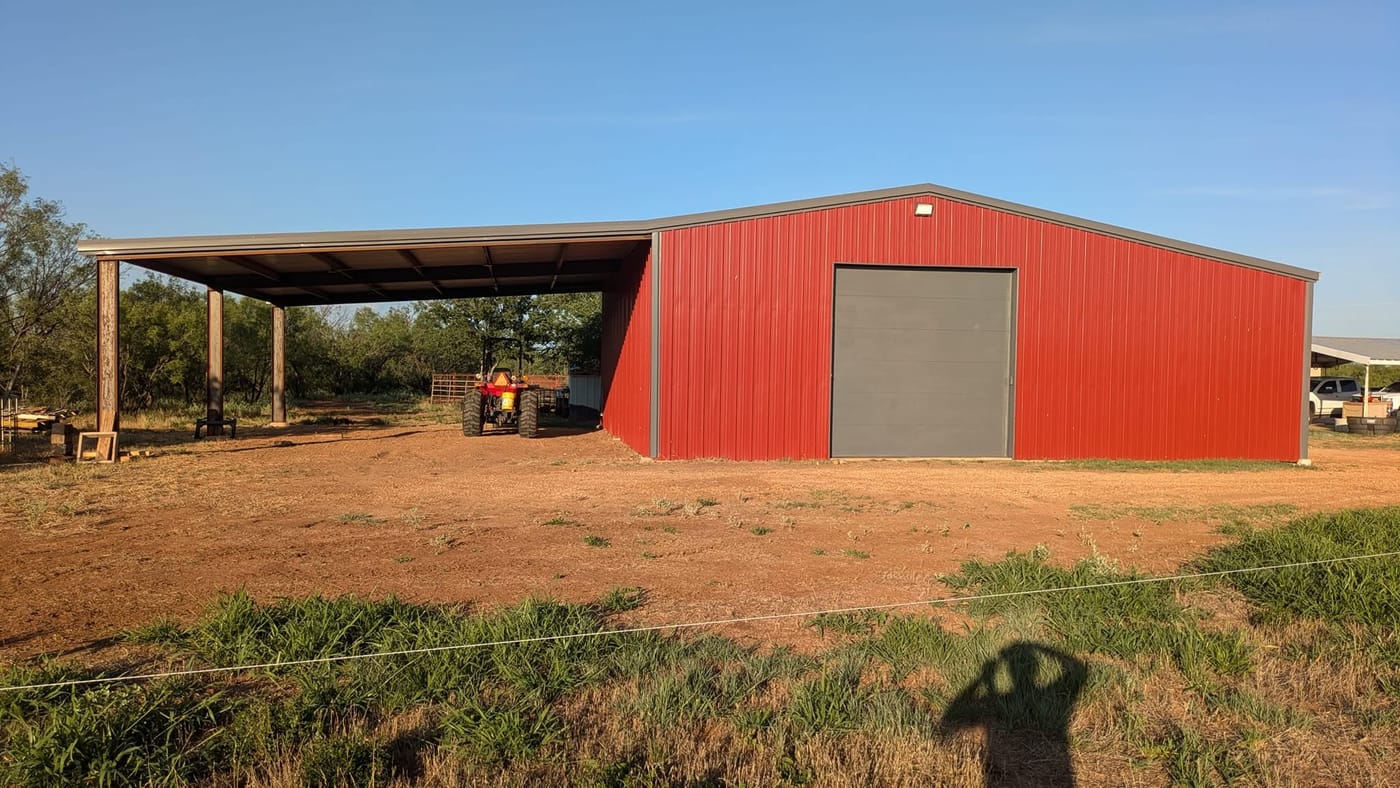 Red steel shop with a grey roll-up door and a covered side porch