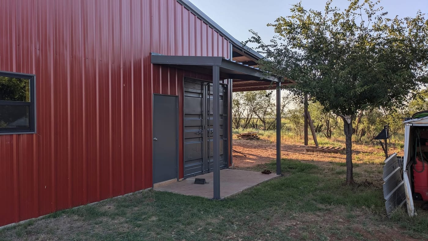 Red steel home with a covered porch beside a tree