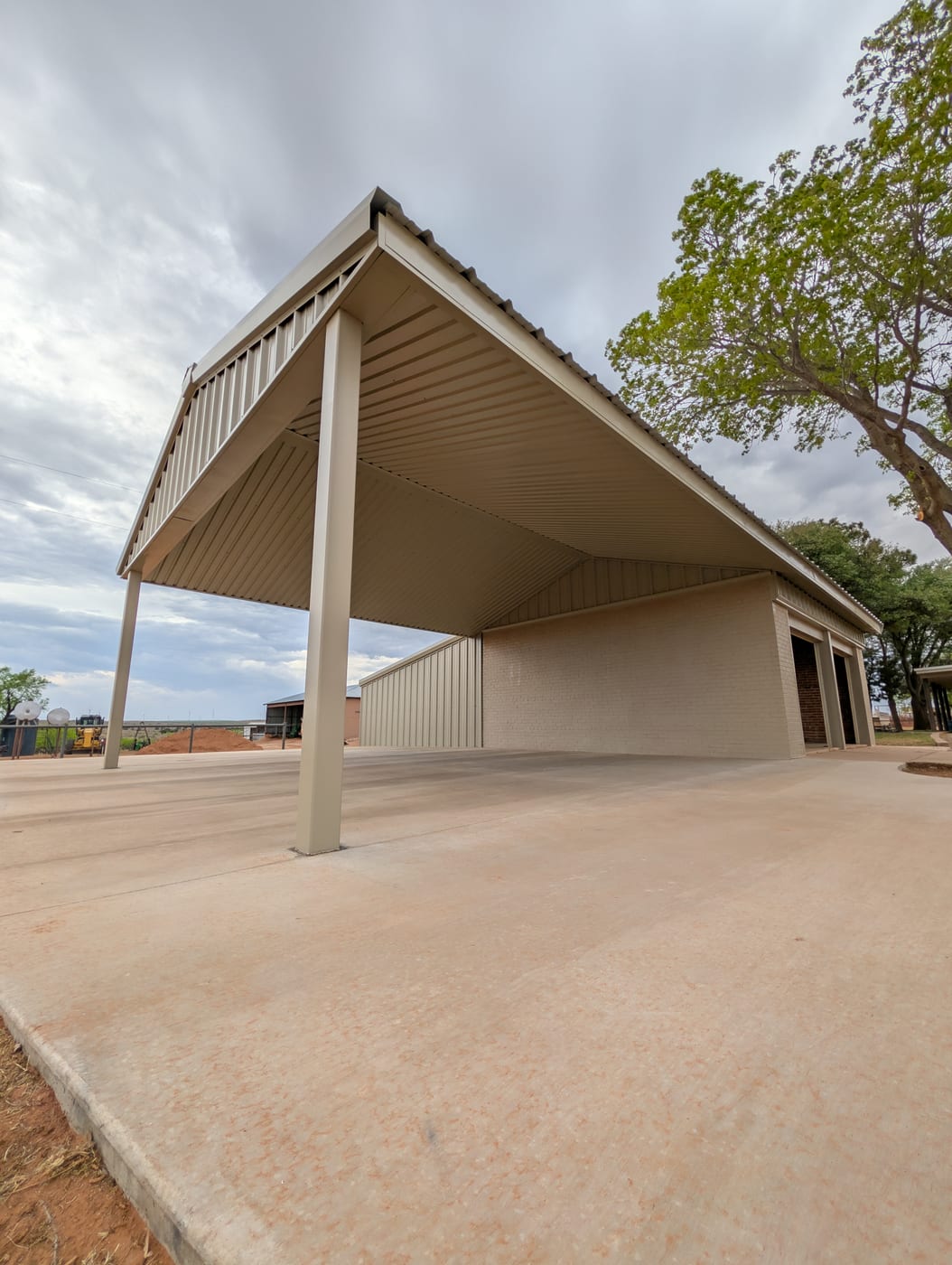 Tan steel pavilion with a tall open-sided roof over a new concrete slab, seen from below