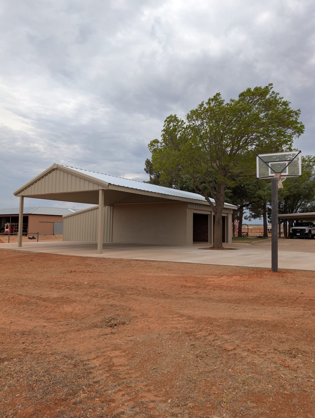 Tan steel pavilion with an attached enclosed shop and a basketball hoop on the slab