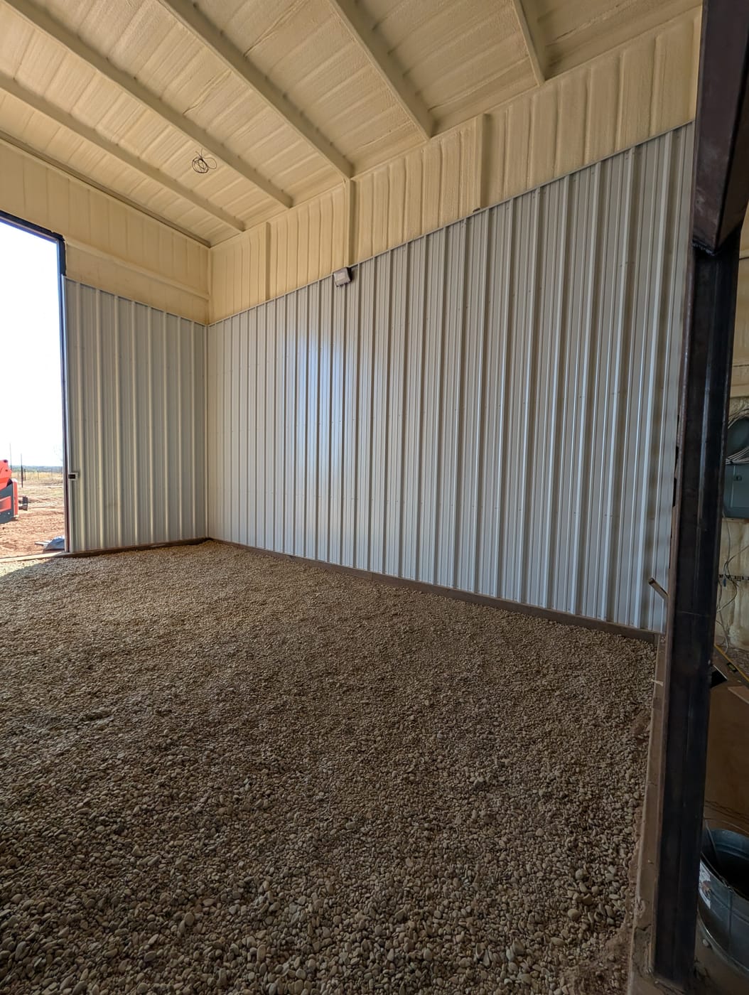 Inside a steel shop with spray foam insulation, a gravel floor and an open roll-up door