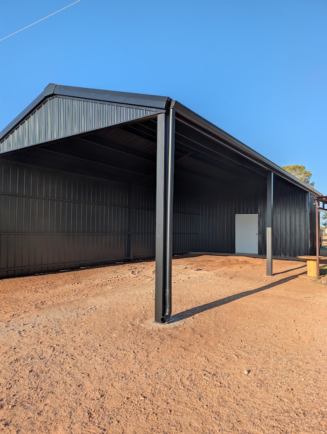 Corner post of a black open-front steel barn casting a long shadow